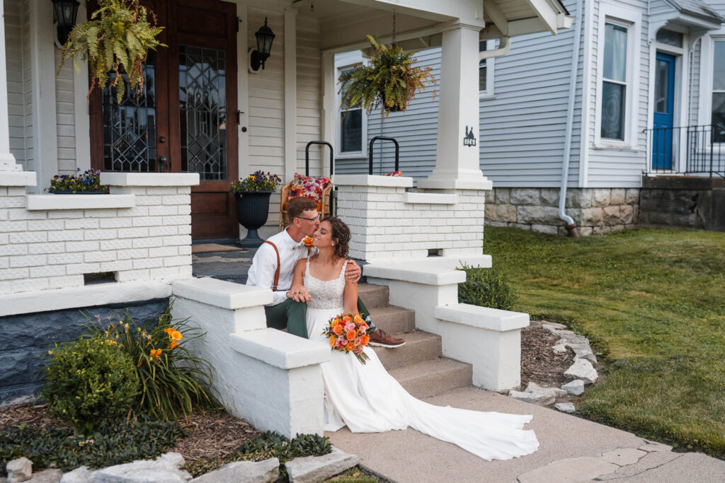 Groom kisses bride on the cheek while sitting on stairs at The Doc's Inn in Greencastle.