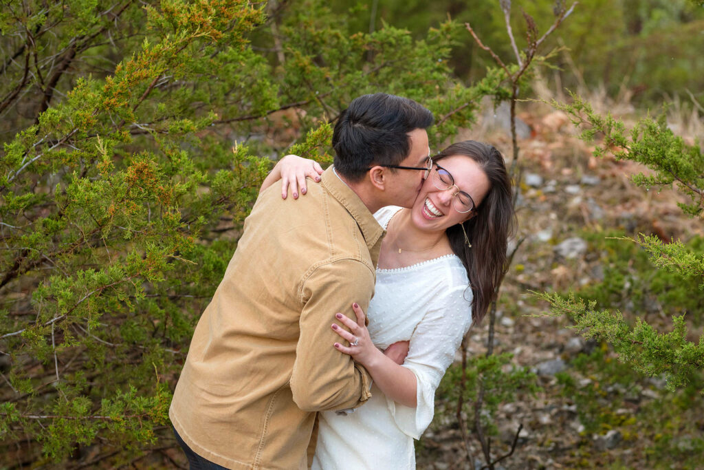 Groom kisses bride on the cheek while she laughs at DePauw Nature Park.