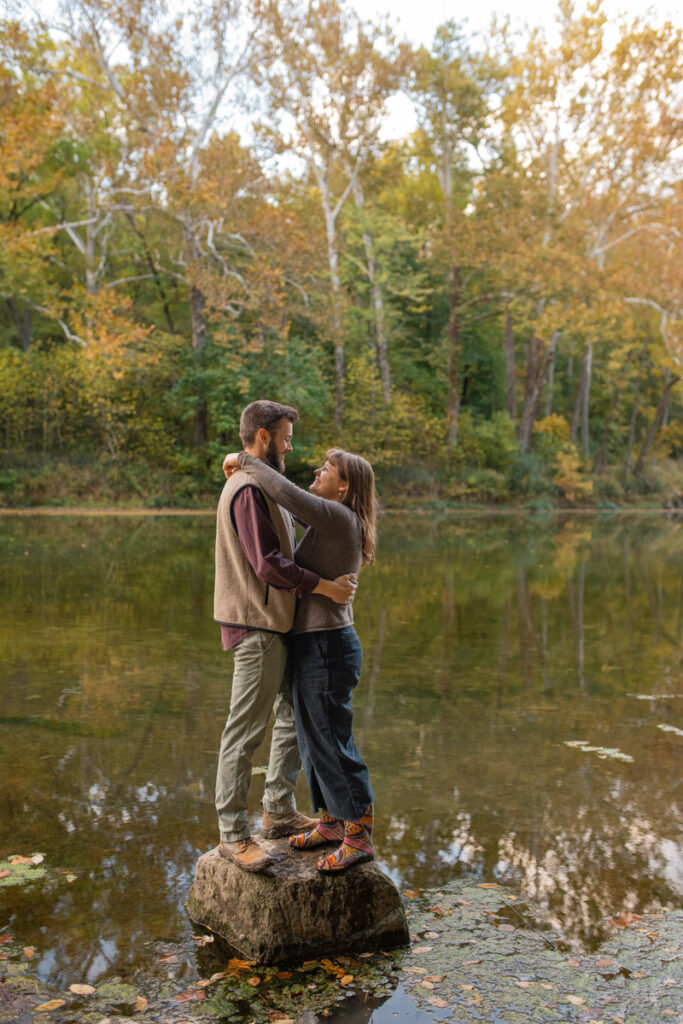 Couple embraces while standing on a boulder in a creek.