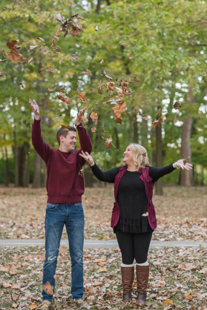 Couple tosses leaves into air while looking at one another.
