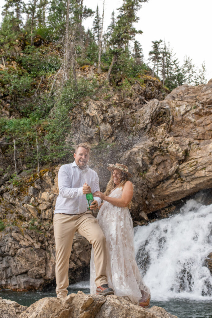 Bride and groom pop sparkling water in front of a waterfall during their elopement.