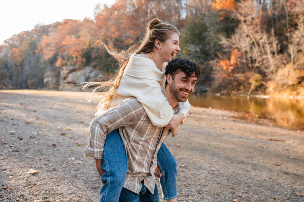 Guy gives girl a bumpy piggyback ride on shore of Sugar Creek at Turkey Run State Park in Indiana.