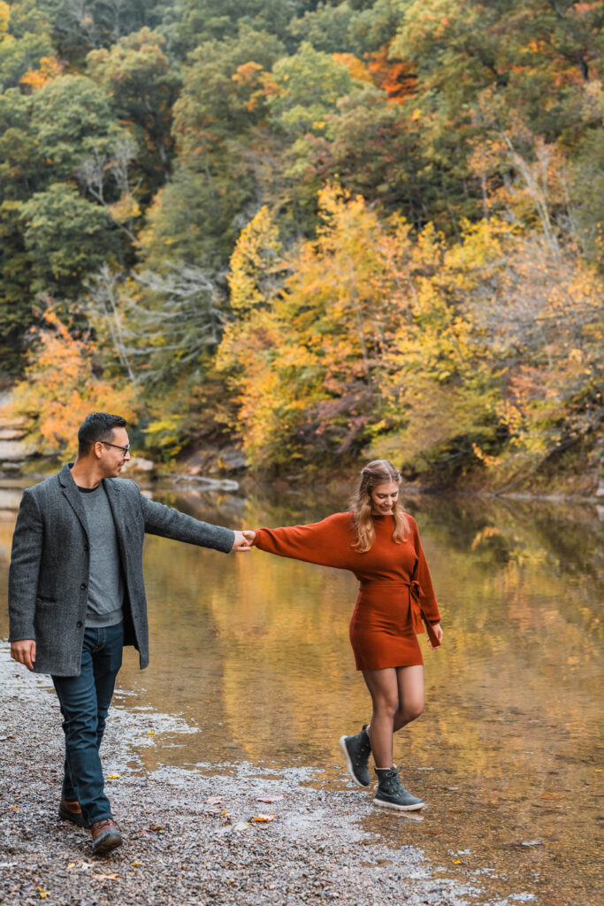 Couple holds hands while walking along a creek bank.