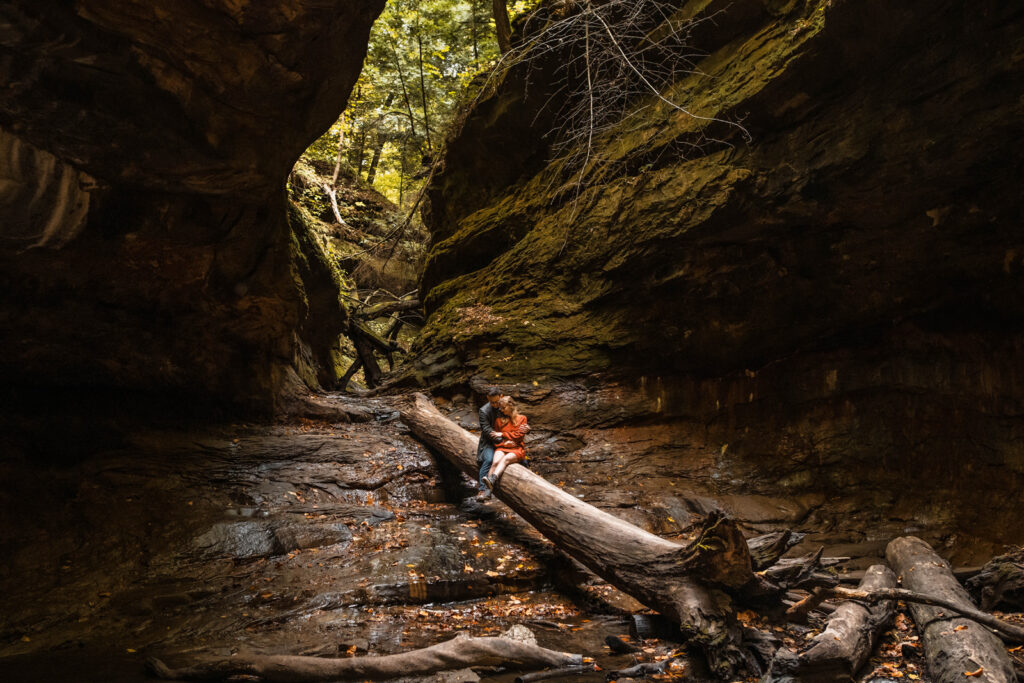 Couple sits on large log in the middle of a giant gorge at Turkey Run State Park in Indiana.