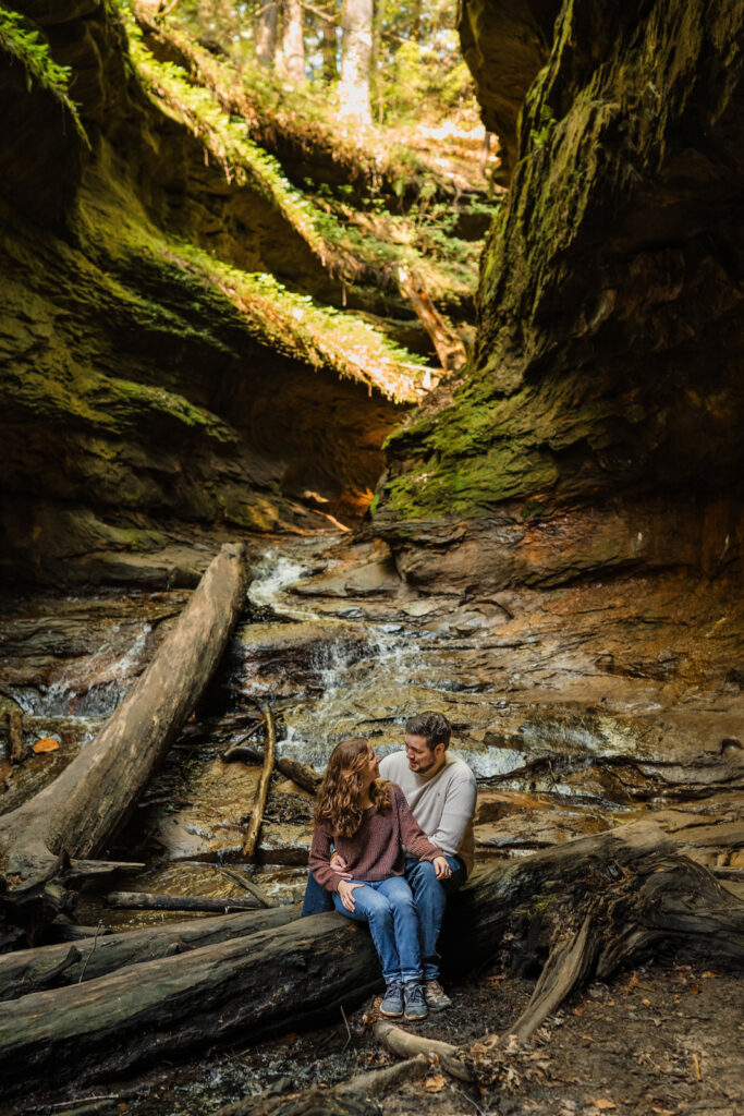 At Turkey Run State Park in Indiana a couple sits on a large log with a waterfall behind them.