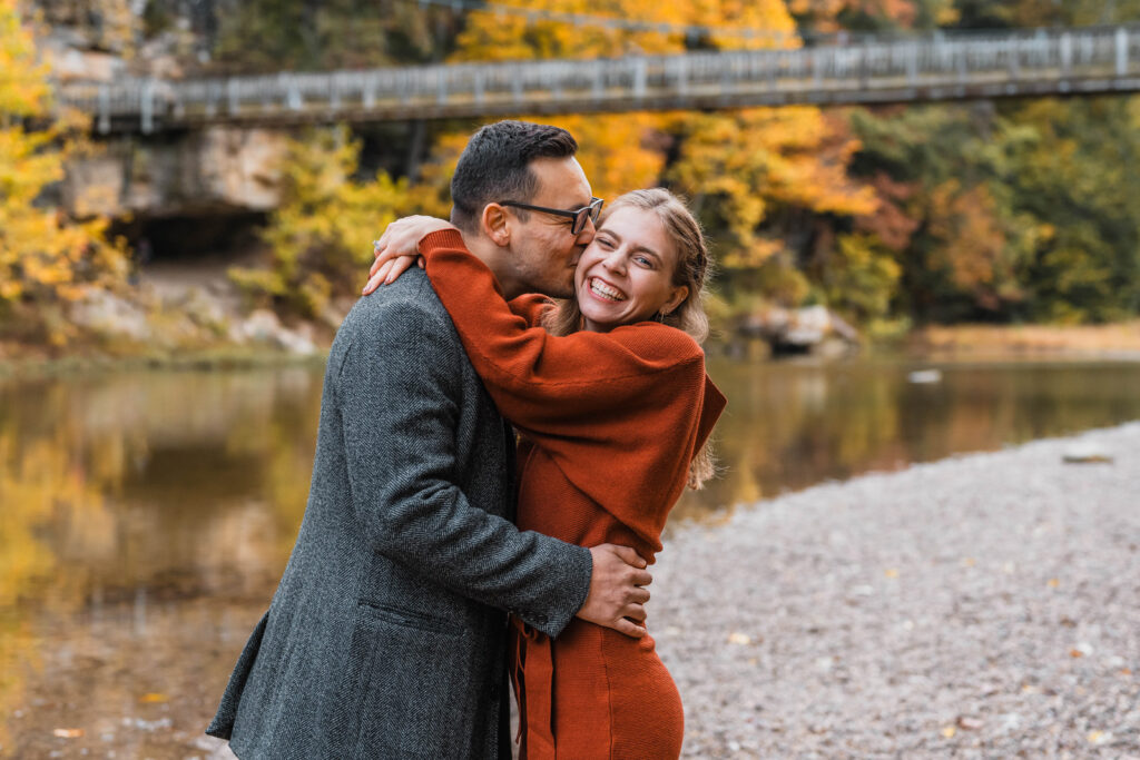 Guy kisses girl on the cheek while she smiles.