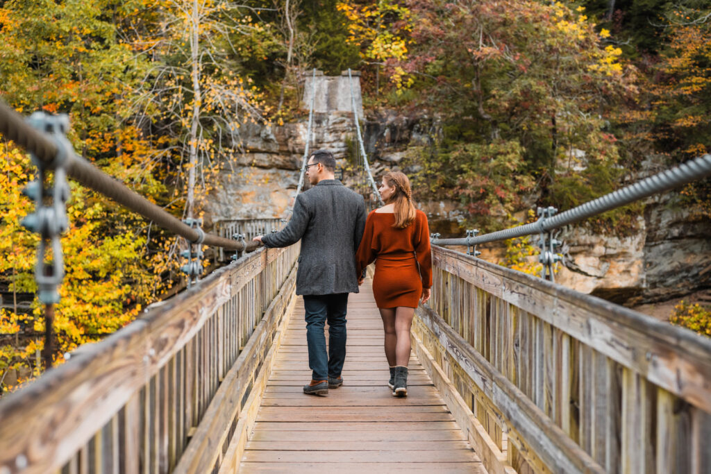 Couple holding hands while walking on suspension bridge.