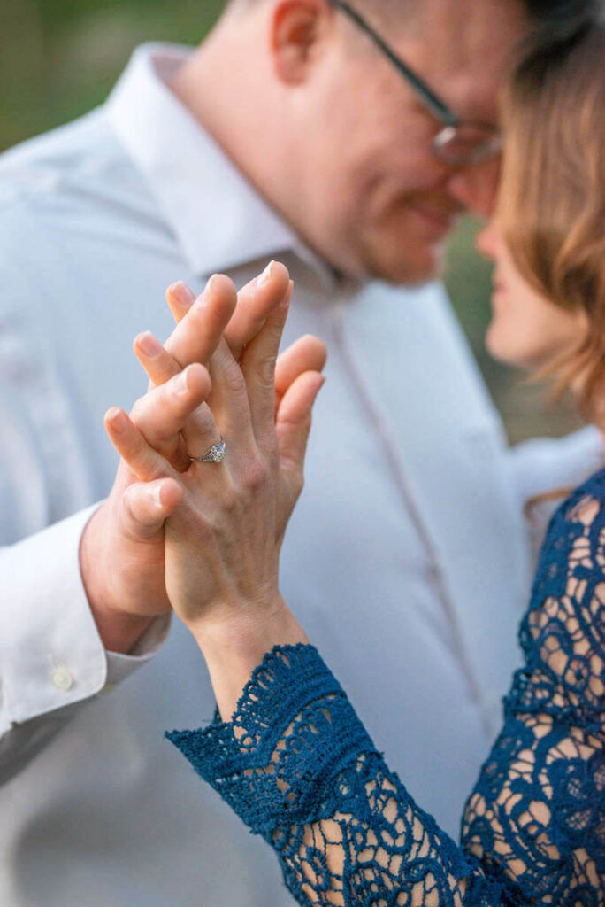 Couple holds hands and woman's engagement ring is in focus.