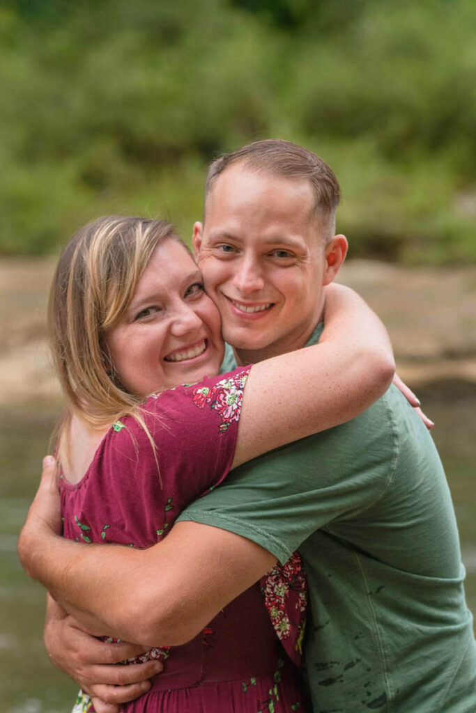 Couple hugging and smiling during waterfall engagement photos.