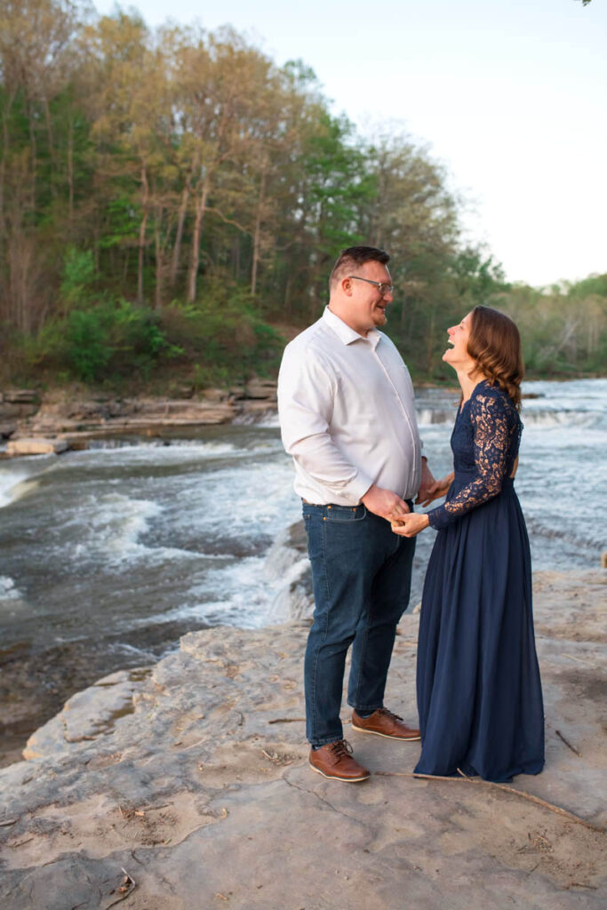 Man and woman holding hands and laughing during waterfall engagement photos.