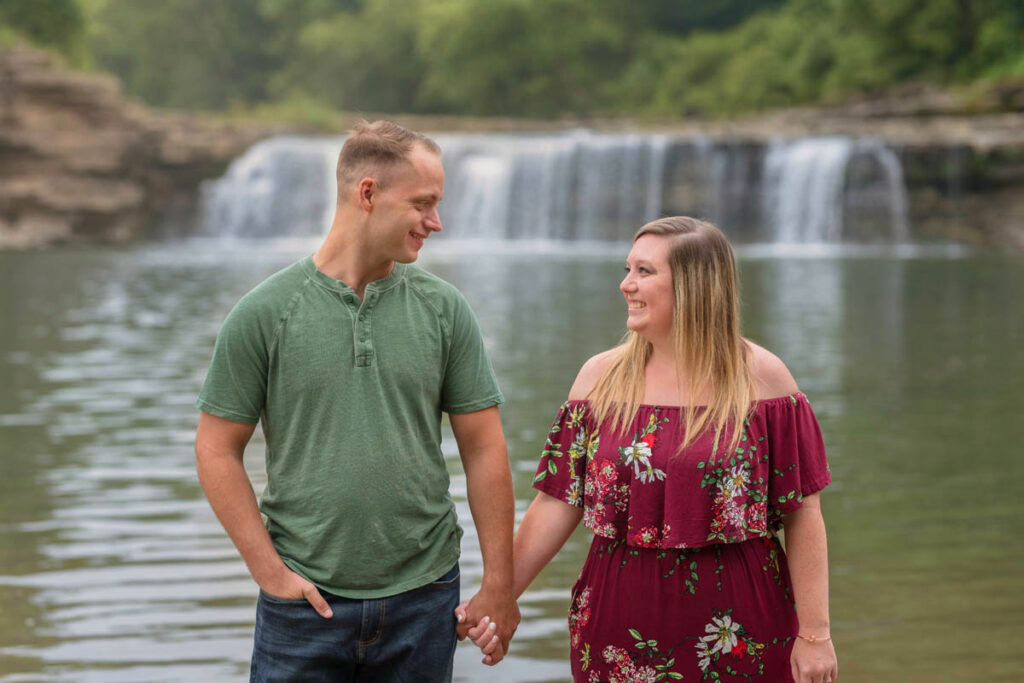 Couple holds hands in front of large waterfall.