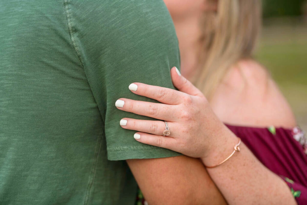 Woman's hand with engagement ring rests on man's bicep.