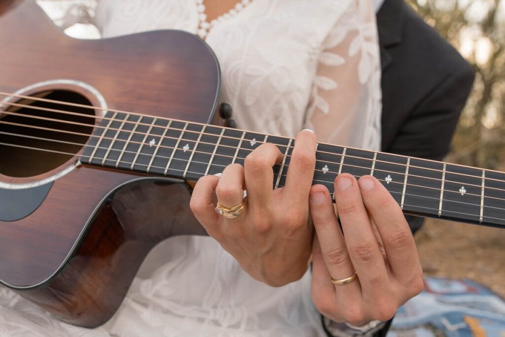 Couple's hands with focus on wedding rings playing on a guitar.