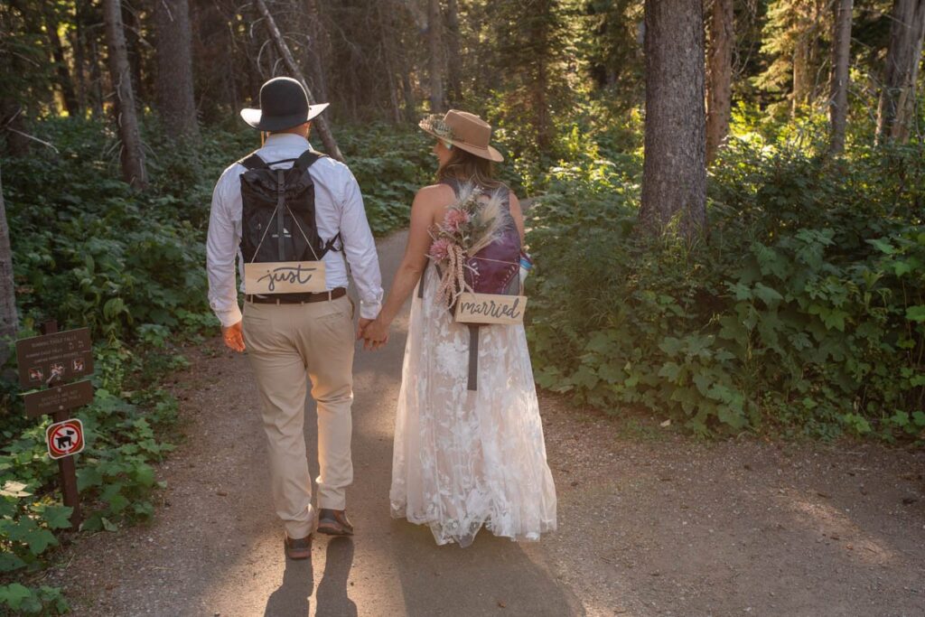 Bride and groom hiking on trail with "Just Married" signs on their backpacks.