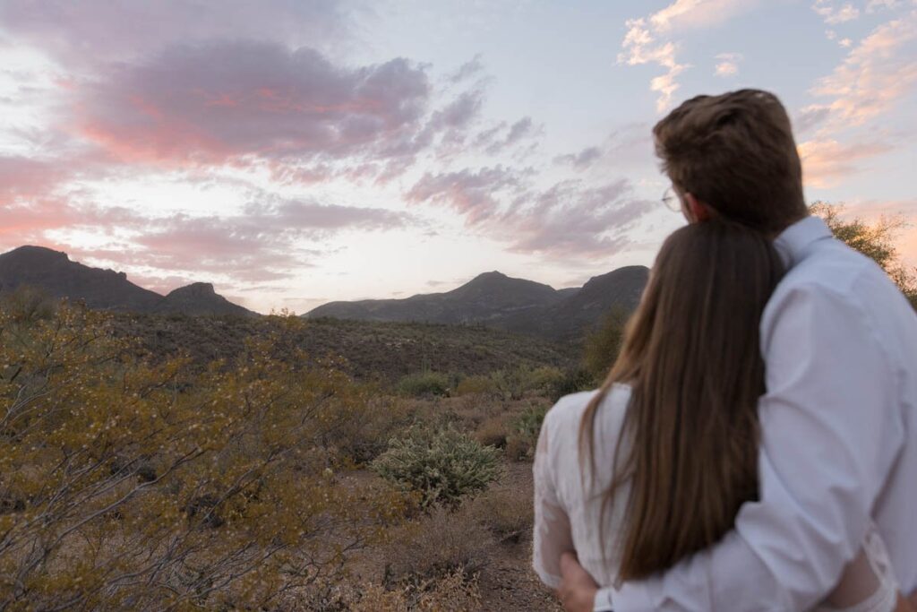 Bride and groom hug looking at sunset over the mountains in Arizona.
