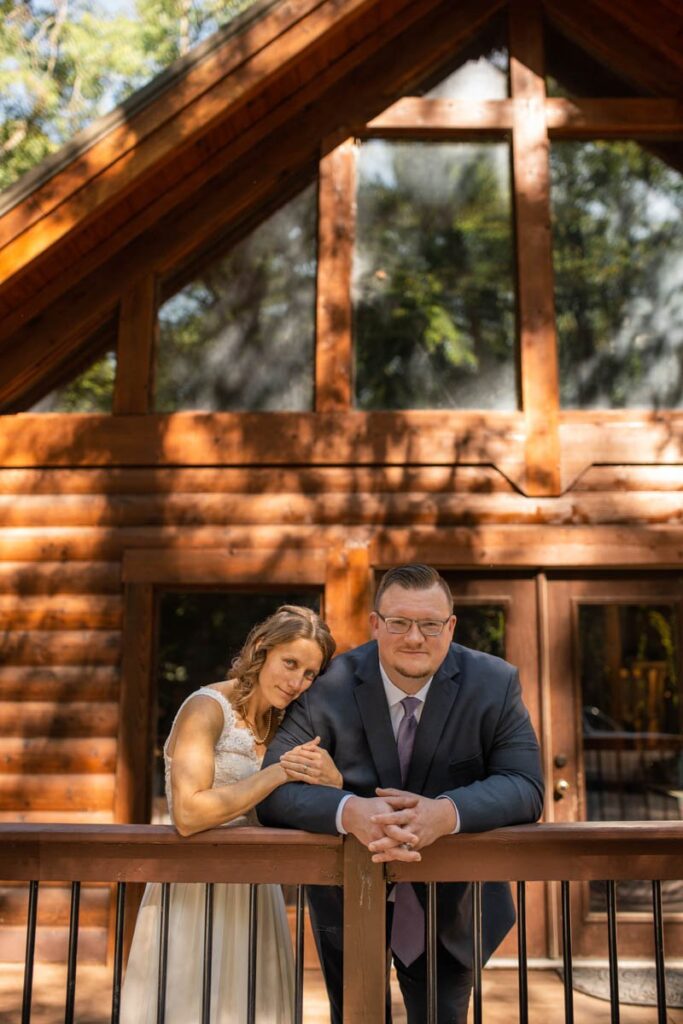 Bride and groom stand together in front of a-frame cabin before their elopement.