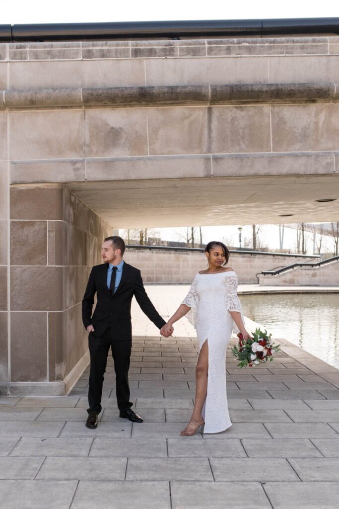 Bride and groom stand next to the canal in Indianapolis holding hands.