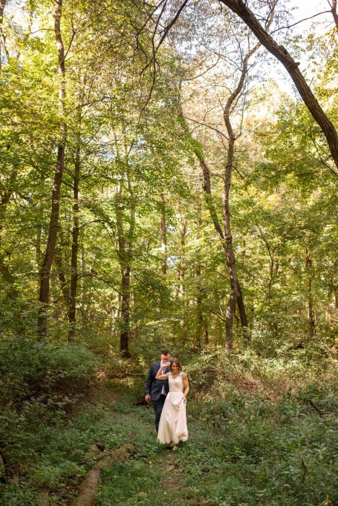 Bride leads groom by the hand on a trail through the woods on their elopement day.