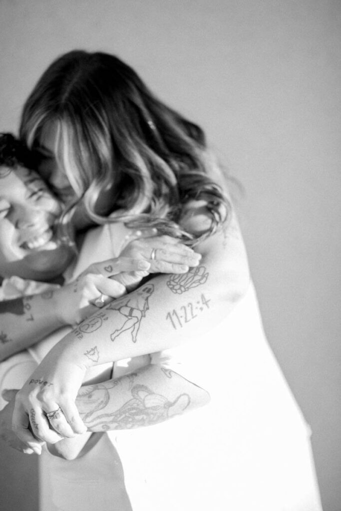 Brides hugging at elopement showing their tattoos on their arms.