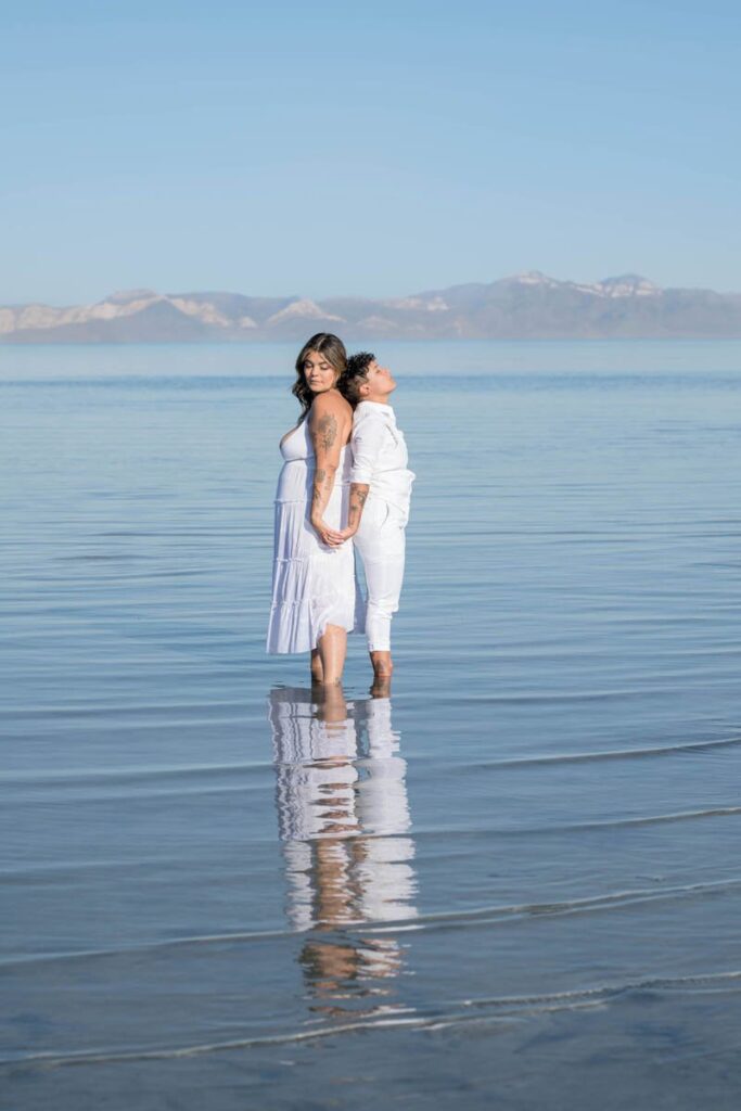 Brides stand with backs together in lake in Utah.