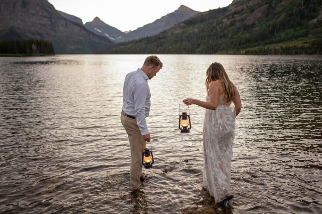 Couple wades into a lake in Montana with lanterns during blue hour.
