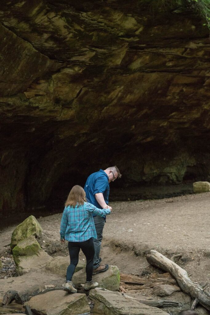 Man holds woman's hand while they cross rocky path at Turkey Run State Park in Indiana.