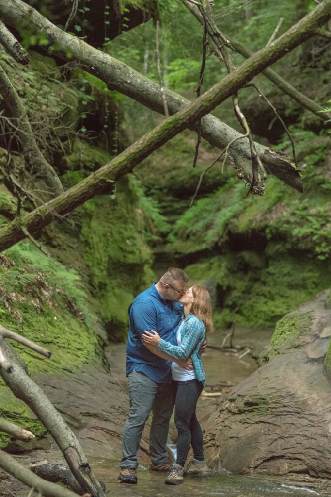Couple kisses during their hike under trees at Turkey Run State Park in Indiana.