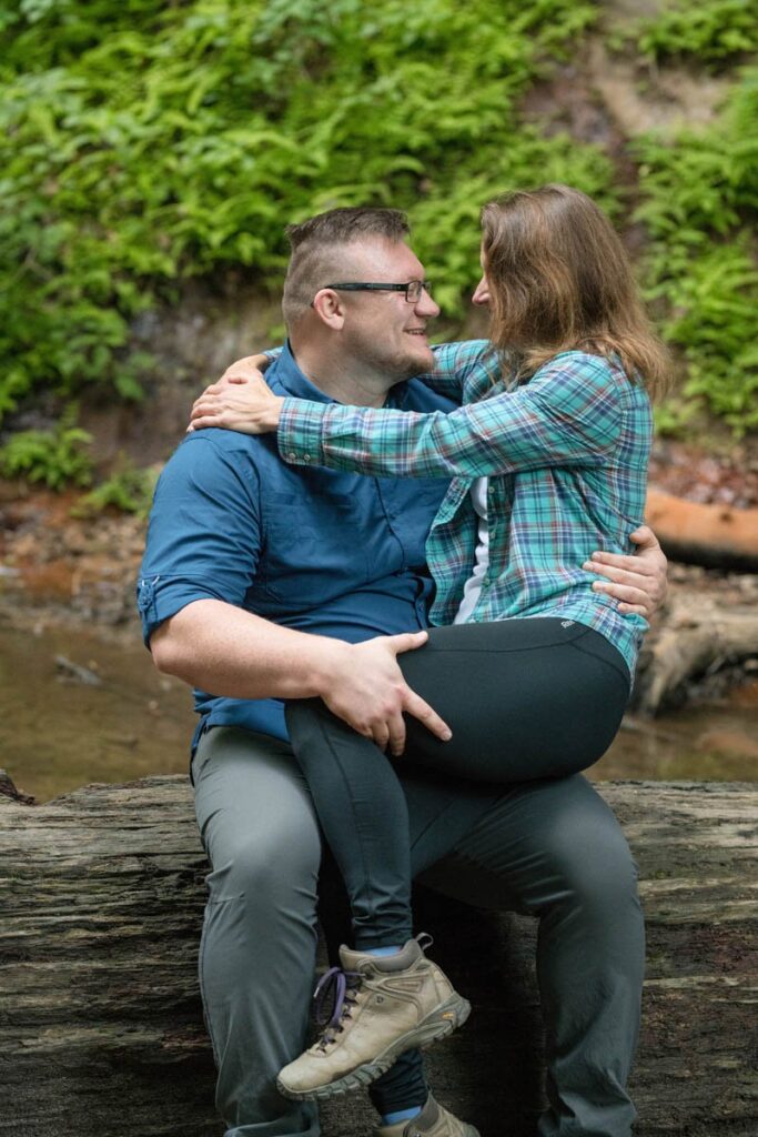 Man and woman sitting together on a fallen log smiling.