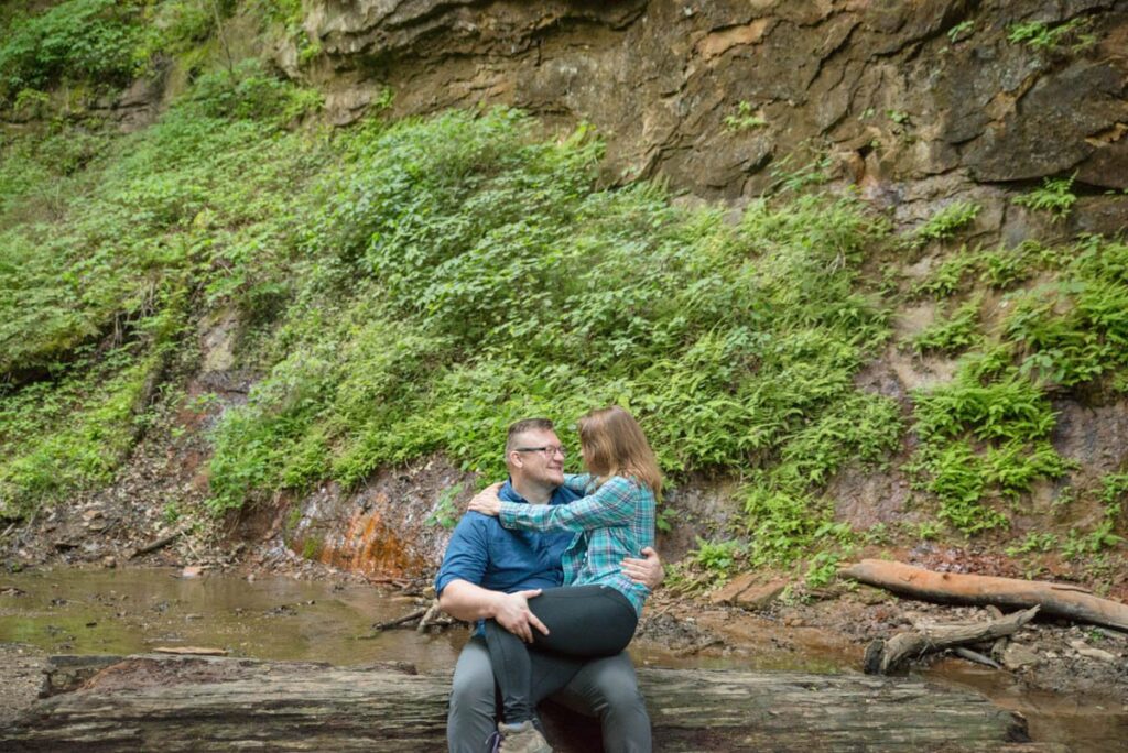 Man and woman are laughing while sitting on a large fallen log together.