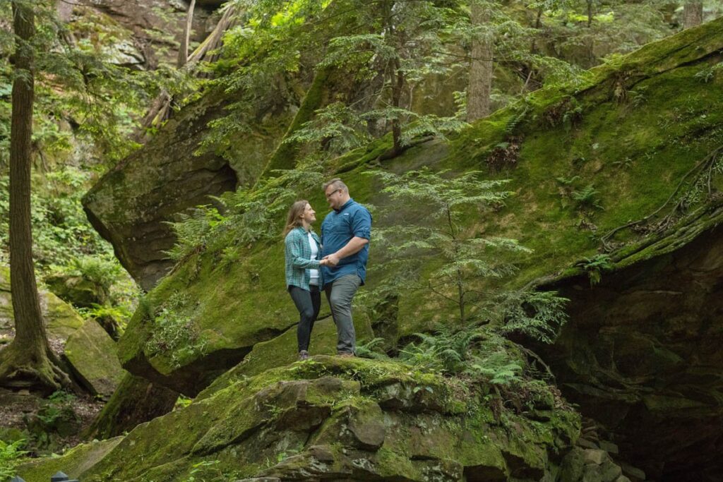 Couple looks at one another while standing on top of a boulder.