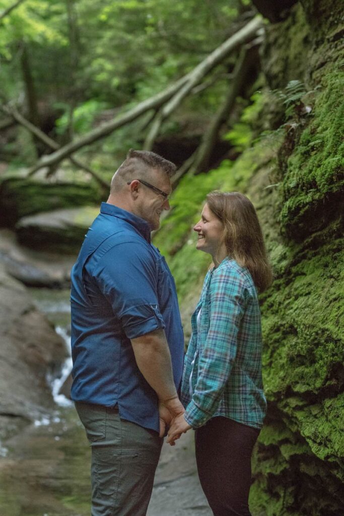 Couple looks at each other while a small stream flows behind them.