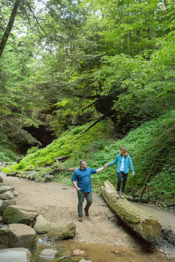 Man holds woman's hand while she walks on large fallen log.