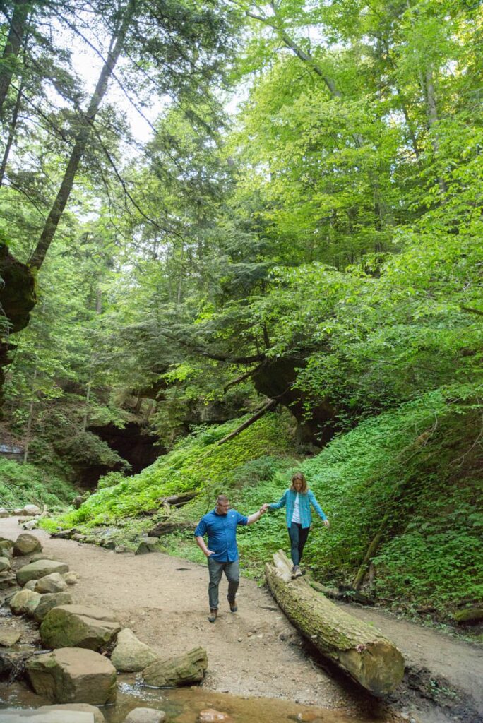 Man holds woman's hand as she walks on top of a large fallen log.