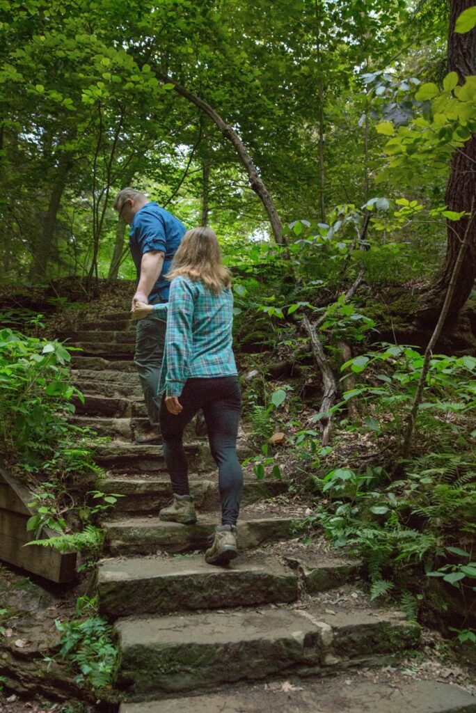 Man leads woman up rocky stairs on hiking trail at Turkey Run State Park in Indiana.