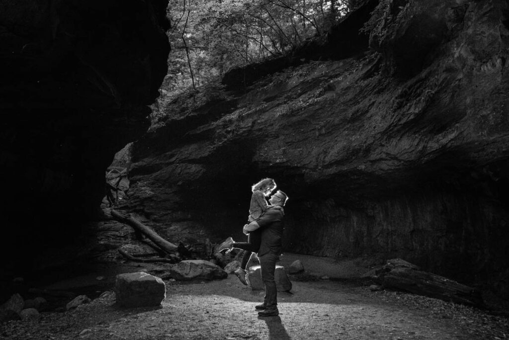 Black and white image of man lifting up woman in a gorge surrounded by rocky walls.