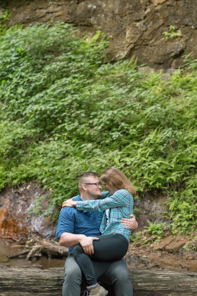 Woman sits with man on a log while smiling and looking at one another.