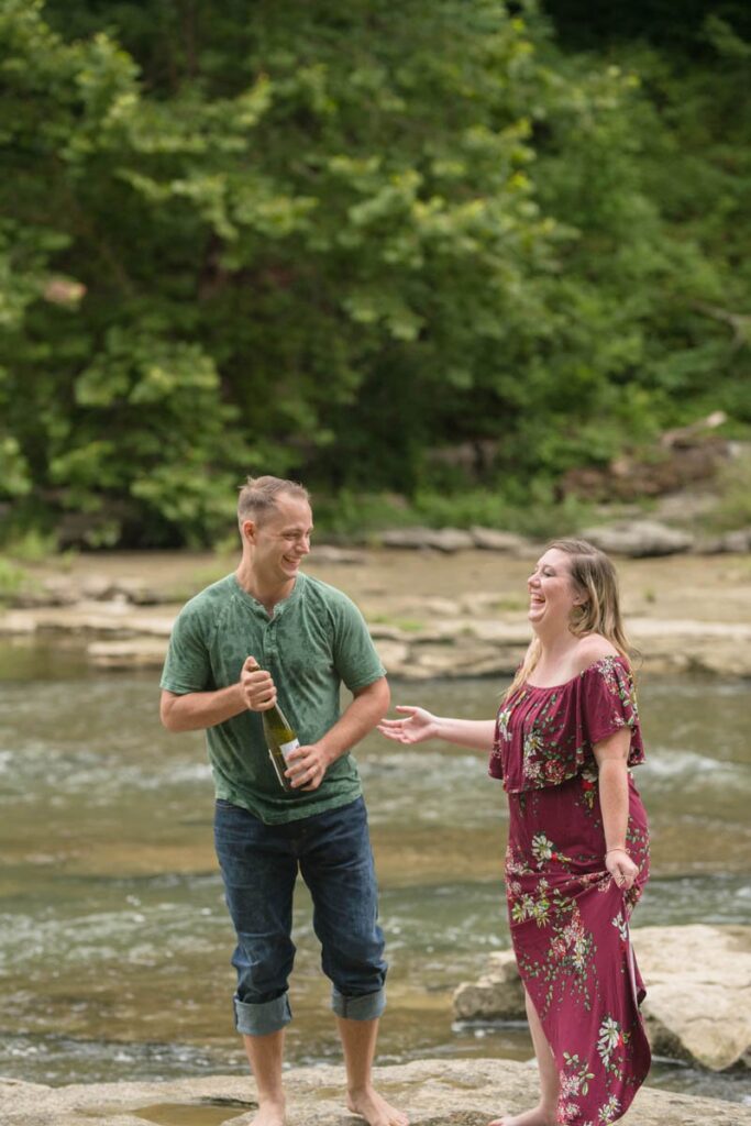 Couple laughs after sparkling water pop during their waterfall engagement photos at Cataract Falls.