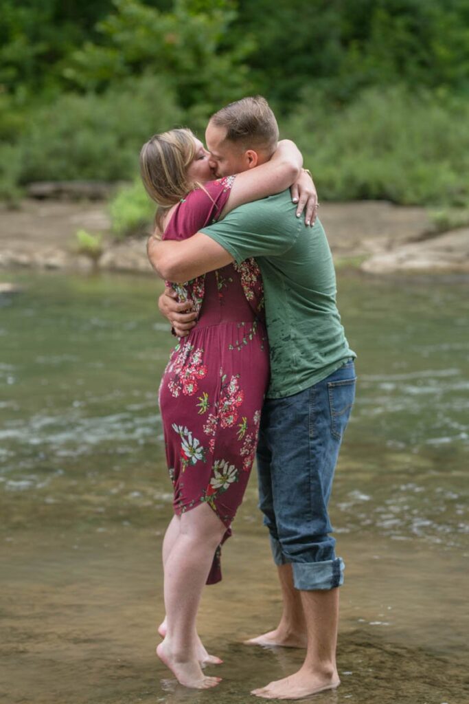 Couple embraces for a kiss while being barefoot in a stream at Cataract Falls State Park.