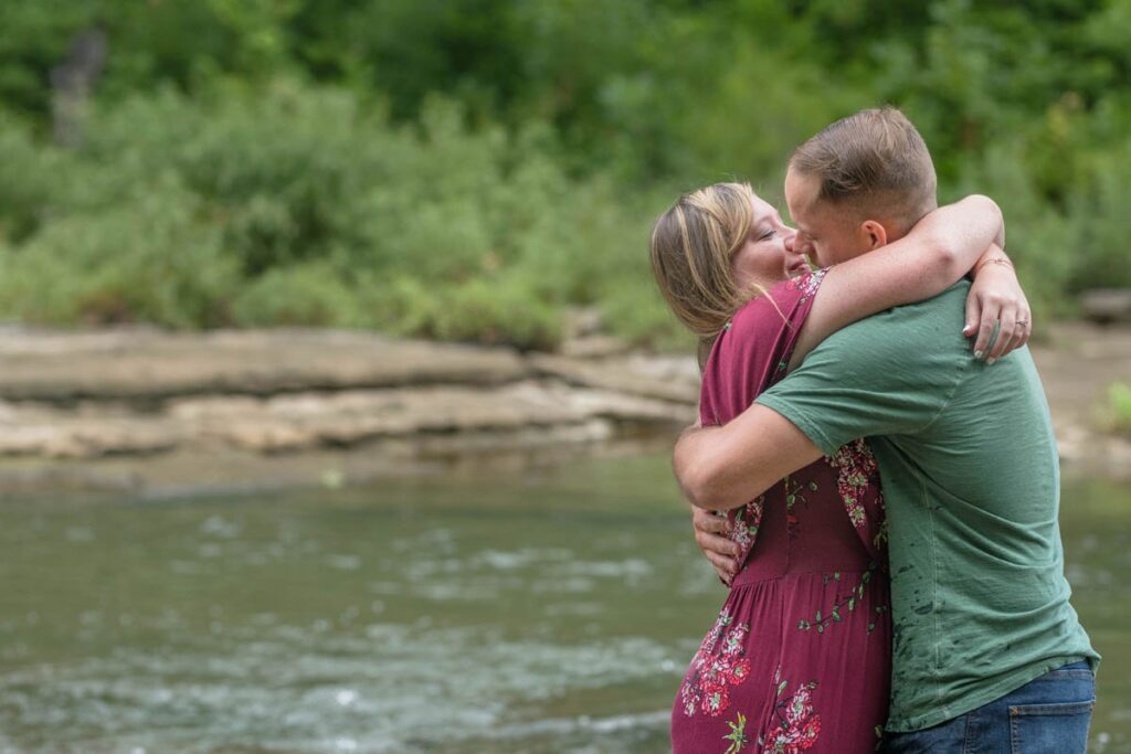 Couple embraces one another for a big kiss while standing in a stream.