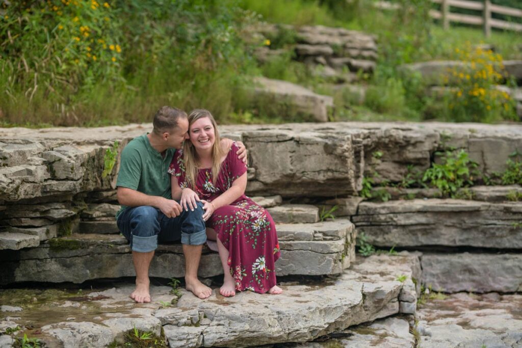 Couple giggles while sitting on rocks together.