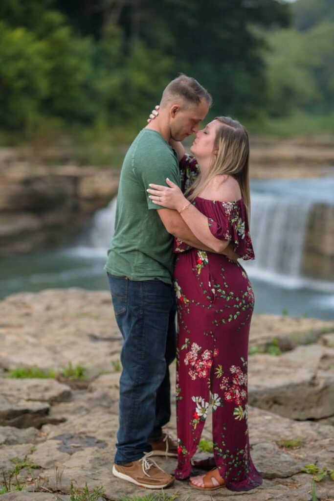 Couple holds each other close during their waterfall engagement photos with Cataract Falls behind them.