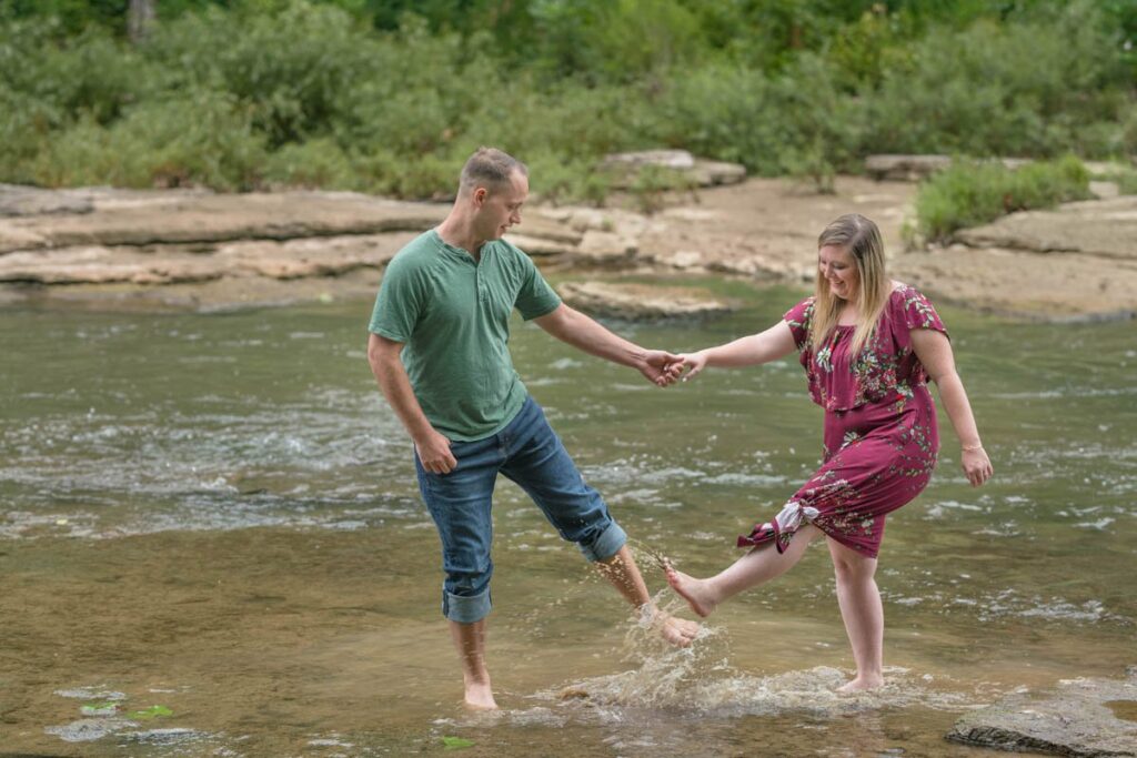 Couple kicks water onto each other during their waterfall engagement photos.