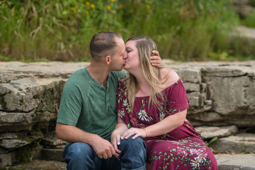 Couple kisses sitting on large rocks.