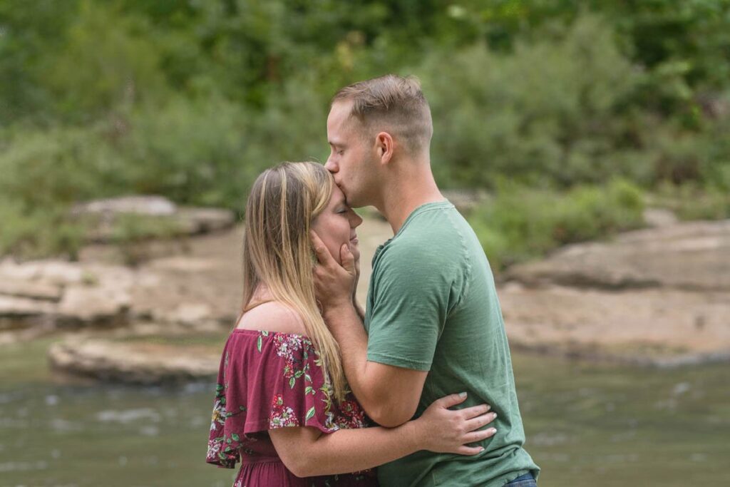 Man kisses woman's forehead while standing in a stream.