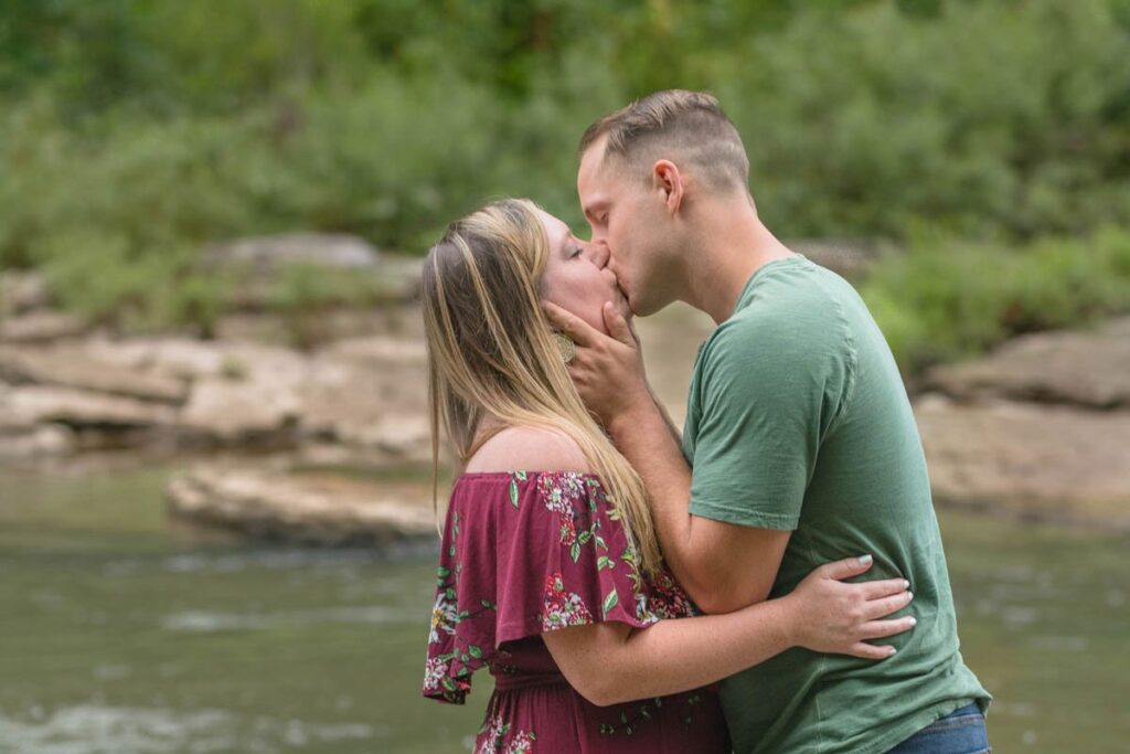 Man pulls woman in for a kiss during their waterfall engagement photos at Cataract Falls.