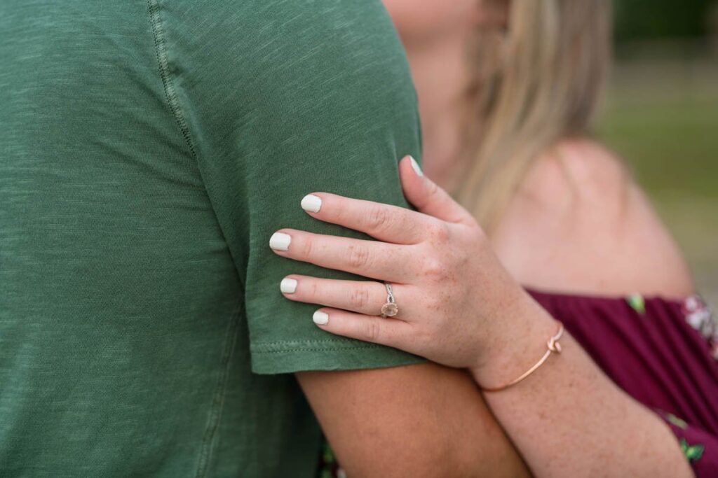 Engagement ring on woman's hand that is hold onto man's bicep. 