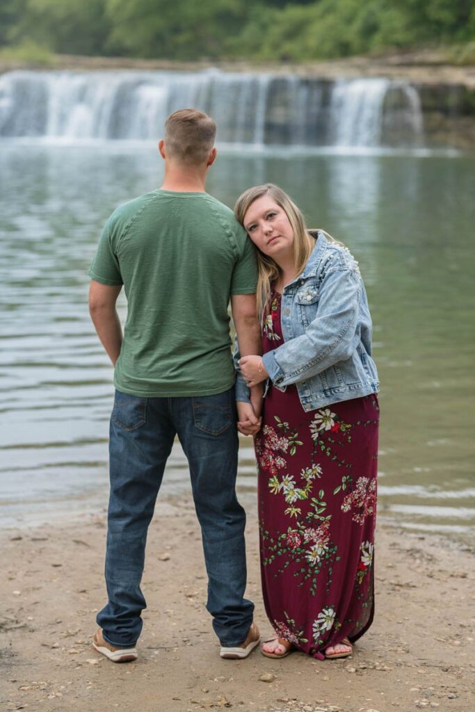 Woman leans on man's shoulder during their waterfall engagement photos.