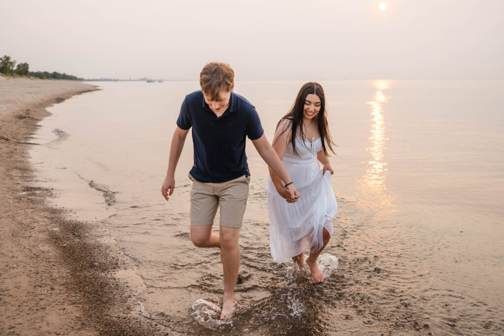 Couple walking hand in hand getting beach engagement photos taken at sunset.