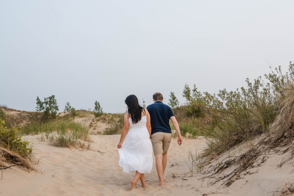 Couple walks up a dune surrounded by beach grass.