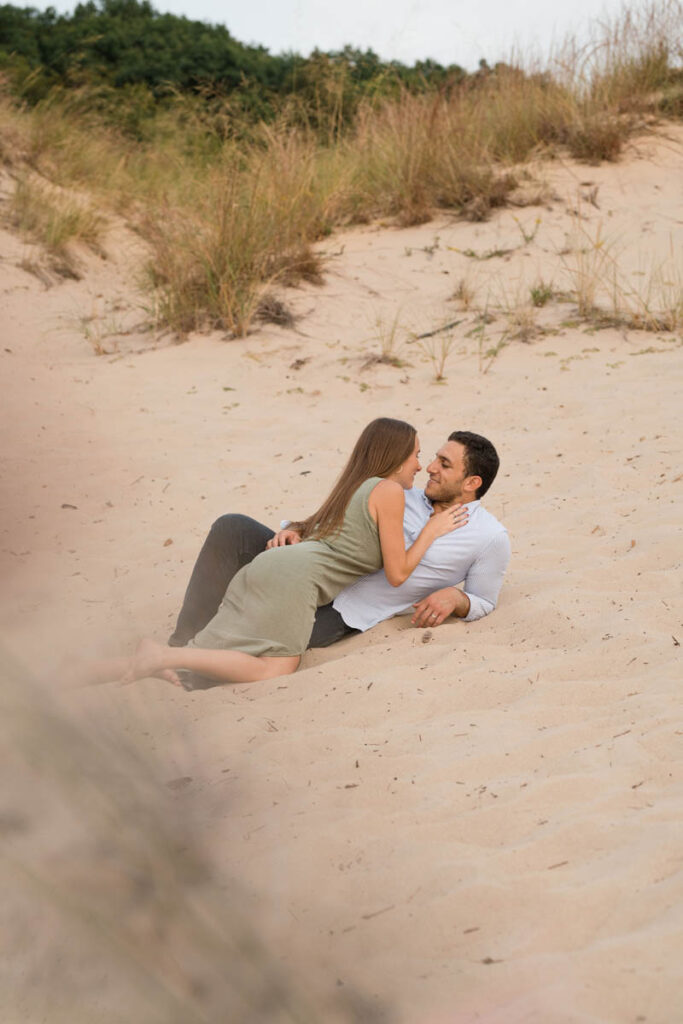 Couple getting ready to kiss laying in the sand during beach couples photography session at Indiana Dunes.